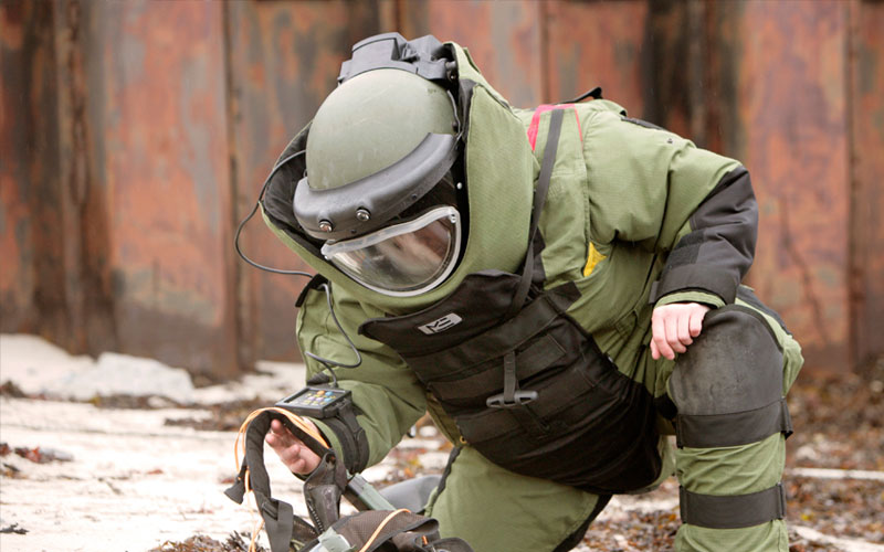 A technician in a full bomb-disposal suit working over equipment during a defence exercise