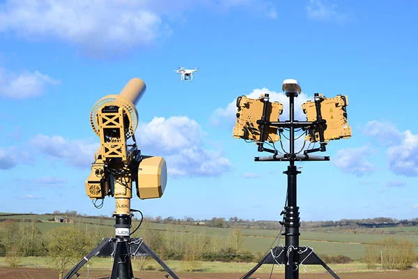 Two mast-mounted anti-drone detection and jamming systems tracking a small UAV over open country